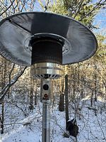 Close-up of propane patio heater top showing wide metal heat dispersing cover, ignition panel and heater mesh.