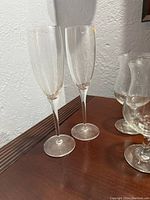 Two clear glass champagne flutes and assorted other stemmed glasses on wooden surface.