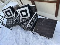 Photo showing two black synthetic wicker armchairs with black and white seat and back cushions, and a matching black wicker side table.