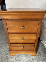 Front view of nightstand showing three drawers with brushed silver knobs, cherry wood finish