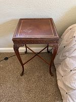 Front side view of one antique leather top wood side table showing detailed carved legs and leather surface with gold trim.