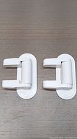 Front view of two identical white plastic child safety locks showing the hinged latch mechanism.