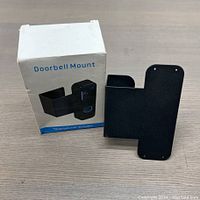 Front view of black metal doorbell mount next to its white box labeled 'Doorbell Mount'