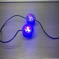 Photo showing two round LED lights emitting red and blue colors, connected by a black cable on a light surface.