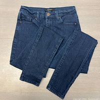 Folded dark blue skinny jeans showing front and leg detail on a wood surface.