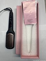 Black Megawise KL-1025 hair straightener brush alongside its original pink box and instruction manual inside.
