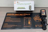 Zegos heating mat box with printed product name and key features, and the flat black heat mat laid out flat showing text instructions and germination chart.