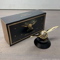 Photo of one Kwak's solar car air freshener with one wing angled backward, placed next to its decorative black and gold box on a wooden surface.