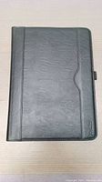 Front view of the black leather tablet case closed, showing the smooth leather surface and subtle stitching.