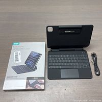 View of ESR Magnetic Keyboard Case box, keyboard case opened, and charging cable coiled beside it on a wood surface.