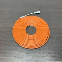Top view of the orange neon flexible strip light coiled on a grey surface with visible connector wire.