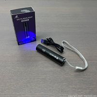 Photo of the UV flashlight alongside USB charging cable and box on a gray surface.