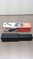 Trailer hitch extender displayed on a table with original box showing product details and images of use