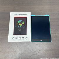 The 12-inch LCD writing board alongside its original box featuring a globe held by hands image and product information.