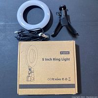 Photo showing 5 inch ring light with attached USB cable, small adjustable black tripod stand, and the original cardboard box marked F-601A 5 Inch Ring Light.