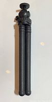 Folded tripod showing textured black legs and ball head adjustment knob at top.