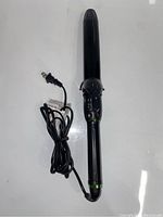 View of black curling iron with power cord and clamp on white background.