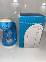 Photo showing the blue and white intelligent foaming soap dispenser next to its box labeled 'Intelligent Sensing Foam Hand Washer (XD-4001)', displaying the product design and packaging.