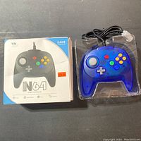 Blue transparent Nintendo 64 game controller in original packaging with original box showing N64 controller print and price sticker.
