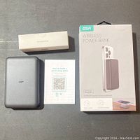 Top-down view showing the power bank, accessories box, user manual, and retail box on a gray surface.