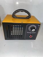 Front view of a rectangular ozone generator machine with yellow top and black front panel, displaying ventilation holes and timing switch dial with red power button.