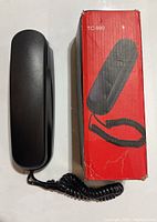 Black slimline telephone handset with coiled cord, shown alongside red box labeled TC-990