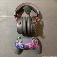 Top-down view of the black Bluetooth headset with red cables and attached microphone, placed above a wireless PS4 controller with a galaxy-style design.