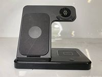 Front angle view of the black 3-in-1 wireless charging station showing smartphone charging pad on vertical section, smartwatch charger on top right, and earbuds charging pad on base.