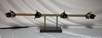Front view of 4-light mid century modern style bathroom light fixture with gold horizontal bar and black light heads on black base.