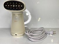 Front view of the handheld garment steamer showing the metal steam plate and power cord wrapped beside the unit.