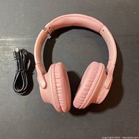 Full view of pink Bluetooth wireless over-ear headphones next to a USB charging cable