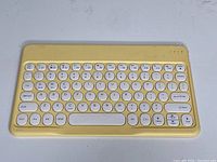 Yellow Bluetooth tablet keyboard with compact design and round keys on a white surface.