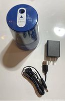 Blue electric pencil sharpener with a transparent top, showing sharpening blades inside, labeled with 6-8mm pencil size indication. Next to it are a black power adapter and a USB cable.