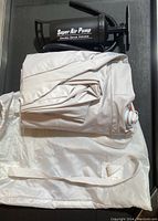 Folded beige inflatable air mattress with visible valves and white carry bag, alongside a black Super Air Pump for inflation.