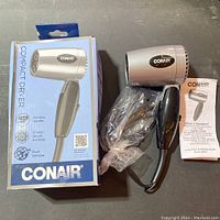 Photo of Conair compact hair dryer with foldable handle, original box, and instruction manual on a flat surface.
