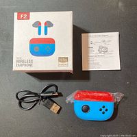 Photo of product box, instruction sheet, charging case in plastic, and USB cable on black surface.