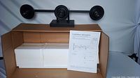 Black modern vanity light fixture with three round mounts/sockets on a horizontal bar, boxed with white styrofoam and installation instructions visible.