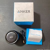 Top view showing the speaker grill with Anker branding, charging cable, owner's manual, and box