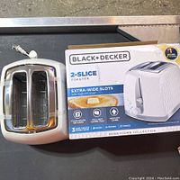 White Black+Decker 2-slice toaster with extra-wide slots next to its product box; box shows key features such as 7 toast shade settings and high-lift lever.