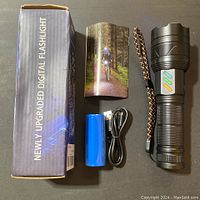 Box labeled Newly Upgraded Digital Flashlight with included flashlight, blue 26650 lithium battery, USB Type-C charging cable and user manual.