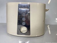 Front view of white Seedeem toaster showing power/functional buttons and browning knob.