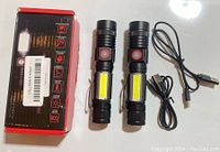 Set of two black tactical lantern flashlights with COB LED panels, two black USB charging cables, and the original product box.