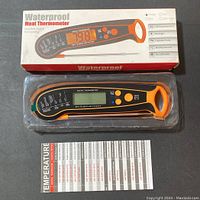 Photo showing the digital waterproof meat thermometer in its packaging with the thermometer display and buttons visible alongside the temperature guide card.