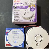 Image of the Kidde wireless smoke and carbon monoxide alarm box, the alarm device and manuals laid out on a surface.