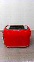 Front angle view showing the red toaster with two slots and smooth glossy finish.