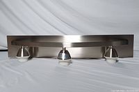 Photo of assembled 3-light bathroom vanity fixture with metal cone-shaped holders on curved bar and rectangular backplate in oil rubbed bronze-black nickel finish