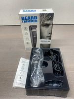 Beard trimmer in plastic tray with charger and instruction manual, next to product box showing branding and features