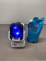 Photo of the bubble machine turned on with blue LED lights and the accompanying party bubble liquid pouch.