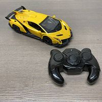 Yellow Lamborghini Veneno miniature remote control car toy with black detailing and a black remote control placed on a wooden surface.