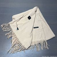 Full view of light beige cashmere scarf with fringed edges, showing the control button and attached rechargeable battery pack with wire.